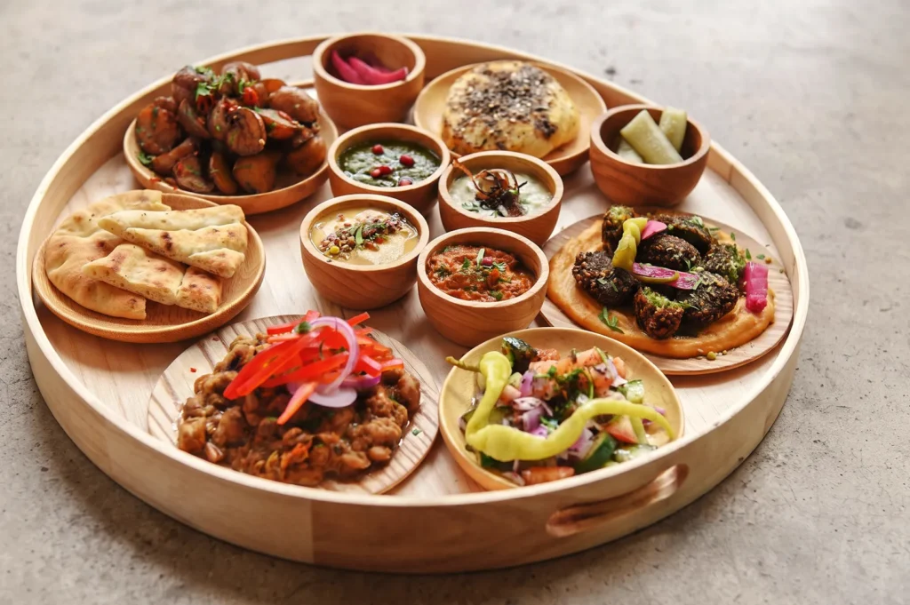 Mediterranean platter with hummus, falafel, flatbread, and assorted dips — a colorful Middle Eastern meal served on a rustic wooden tray.