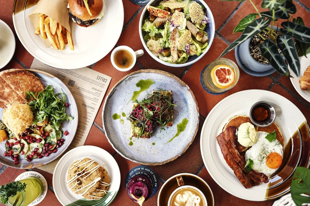 Colorful brunch table featuring pancakes, salad, burger, fries, and espresso — a lively café meal showcasing fresh ingredients and artisanal plating.