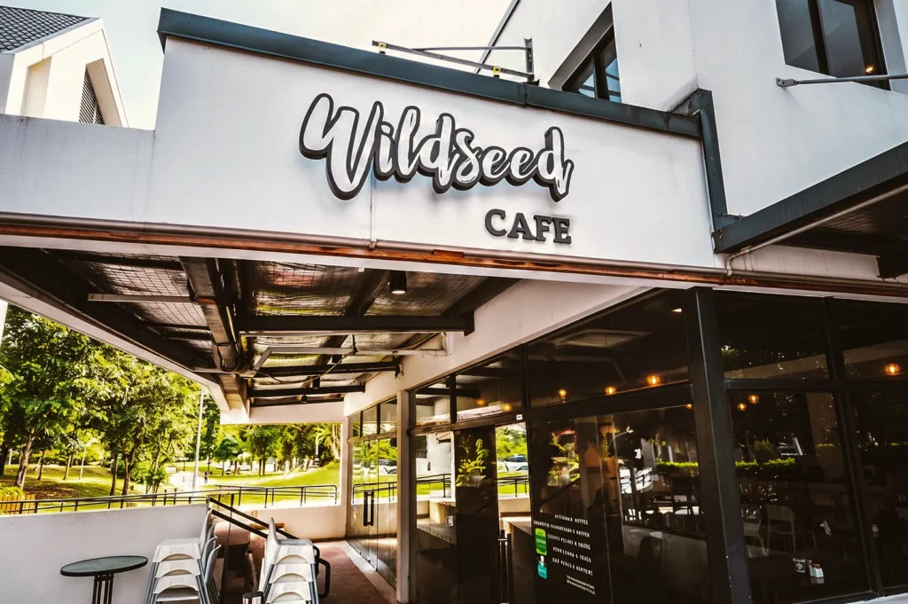 Exterior of Wildseed Café with modern white façade, outdoor seating, and lush greenery — a serene spot for coffee and brunch in a garden setting.