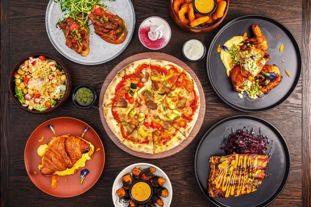 Gourmet meal spread with pizza, croissant sandwich, salad, and roasted chicken — vibrant restaurant dishes highlighting international flavors and presentation.