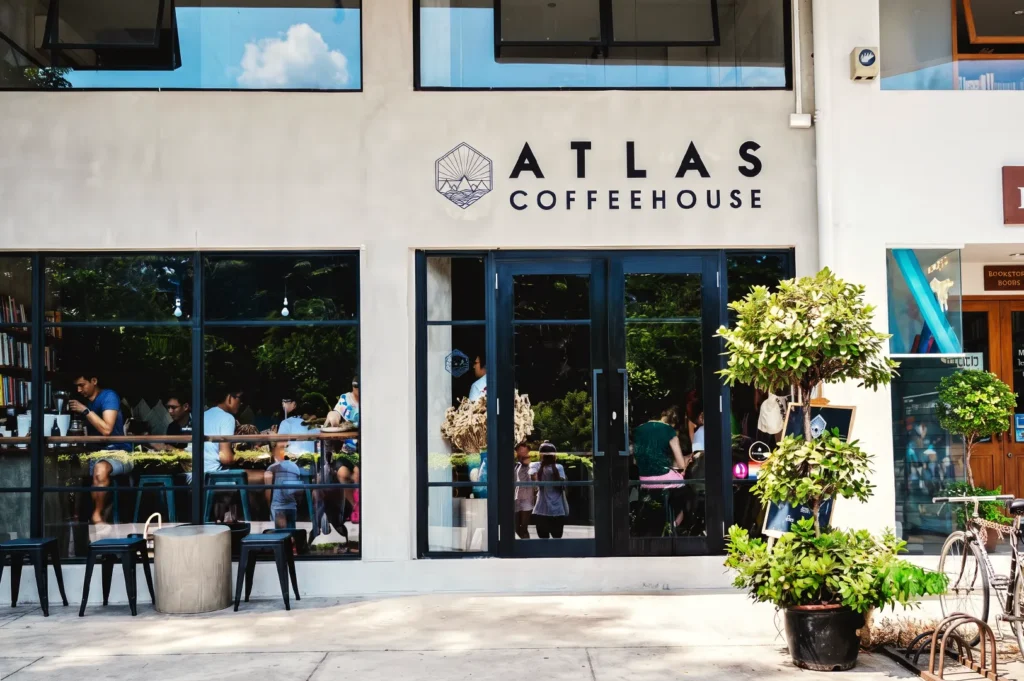 Atlas Coffeehouse exterior with glass windows, modern signage, and customers enjoying coffee — a trendy Singapore café known for specialty brews.
