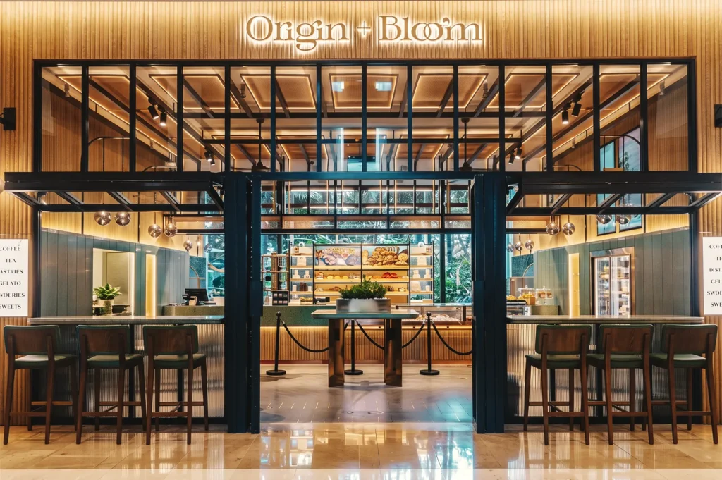 Origin + Bloom Singapore café with modern wood‑and‑glass design, illuminated bakery shelves, and cozy seating.