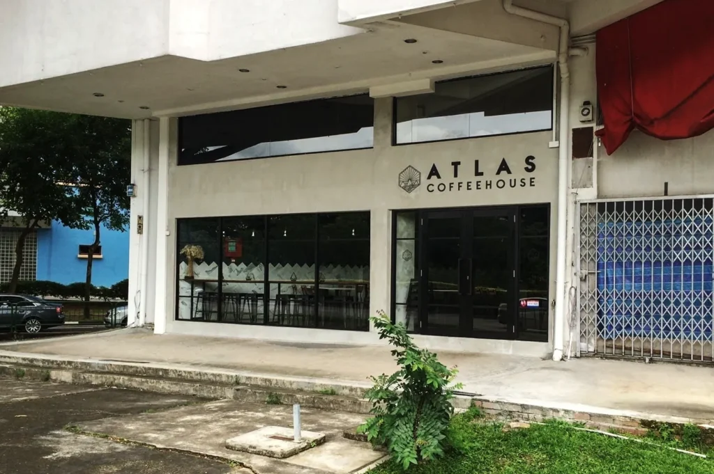 Exterior view of Atlas Coffeehouse Singapore with minimalist concrete façade, large glass windows, and modern black signage in an urban setting.