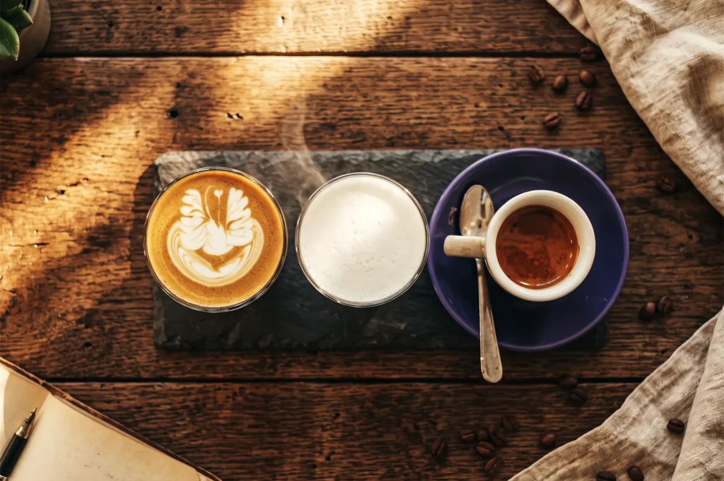 Artistic coffee trio at Atlas Coffeehouse Singapore showing latte with swan art, steamed milk, and espresso on rustic wooden table with coffee beans.