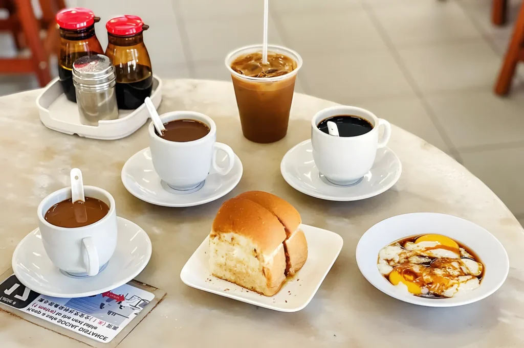 Classic Singaporean breakfast at YY Kafei Dian with kopi coffee, kaya toast, soft‑boiled eggs, and iced coffee on marble table — authentic local café experience.