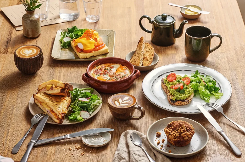 Gourmet brunch setup with avocado toast, soup, grilled sandwiches, and latte art coffee served on a rustic wooden table in a Singapore café.