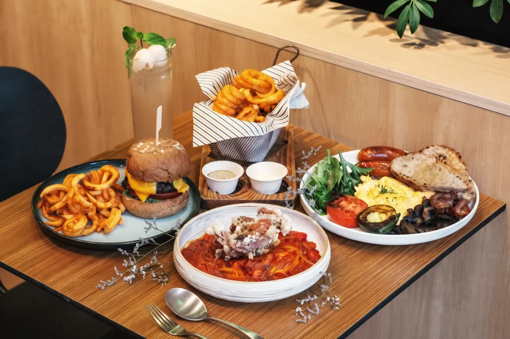 Table spread at Wildseed Café with gourmet dishes including a cheeseburger with curly fries, soft‑shell crab pasta, and a hearty breakfast platter served with fresh greens and toast.
