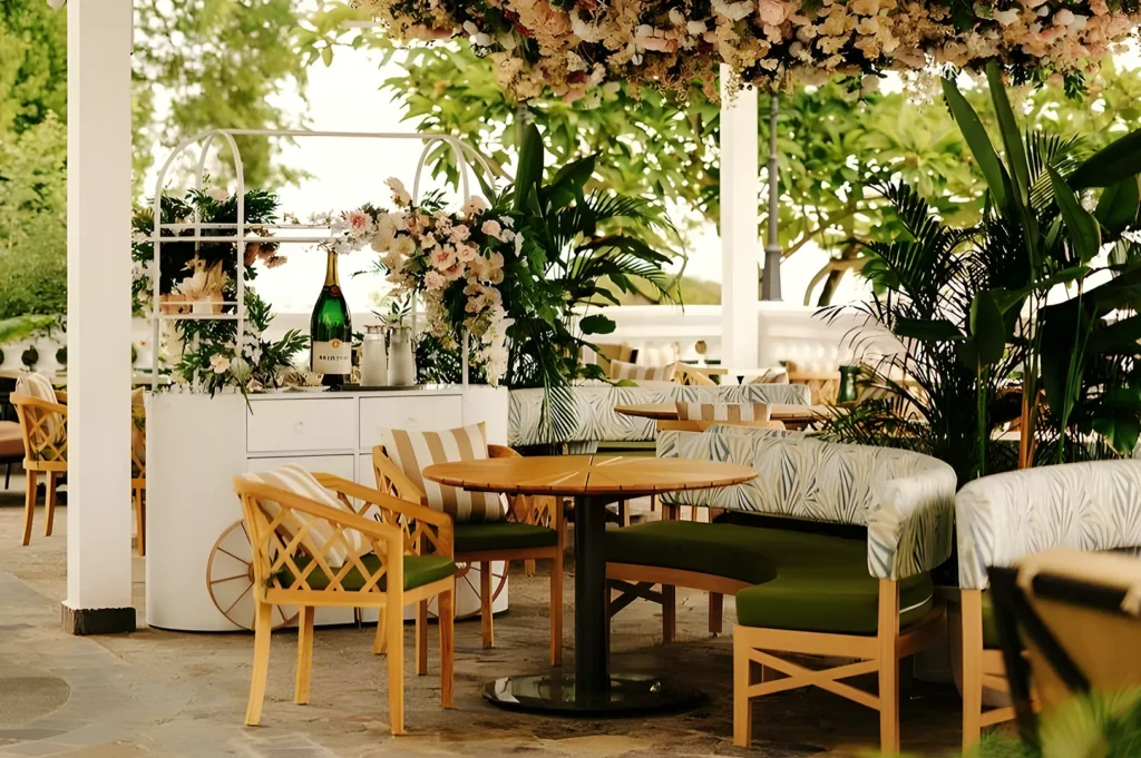 Elegant outdoor dining area at Wildseed Café decorated with floral arrangements, champagne display, and tropical plants, offering a cozy garden‑style ambiance for brunch or coffee.