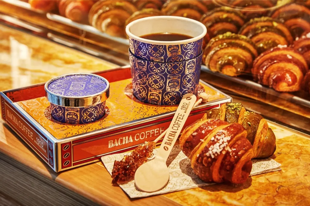 Bacha Coffee Singapore serving premium brew in ornate blue cup with golden accents, paired with glazed croissants and rock sugar stirrer.