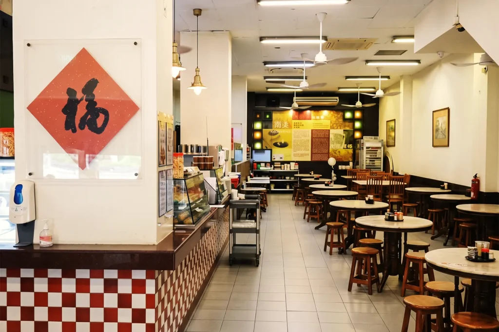 Spacious YY Kafei Dian dining area with marble tables, wooden stools, and red‑and‑white checkered counter — nostalgic Singapore coffee shop atmosphere.