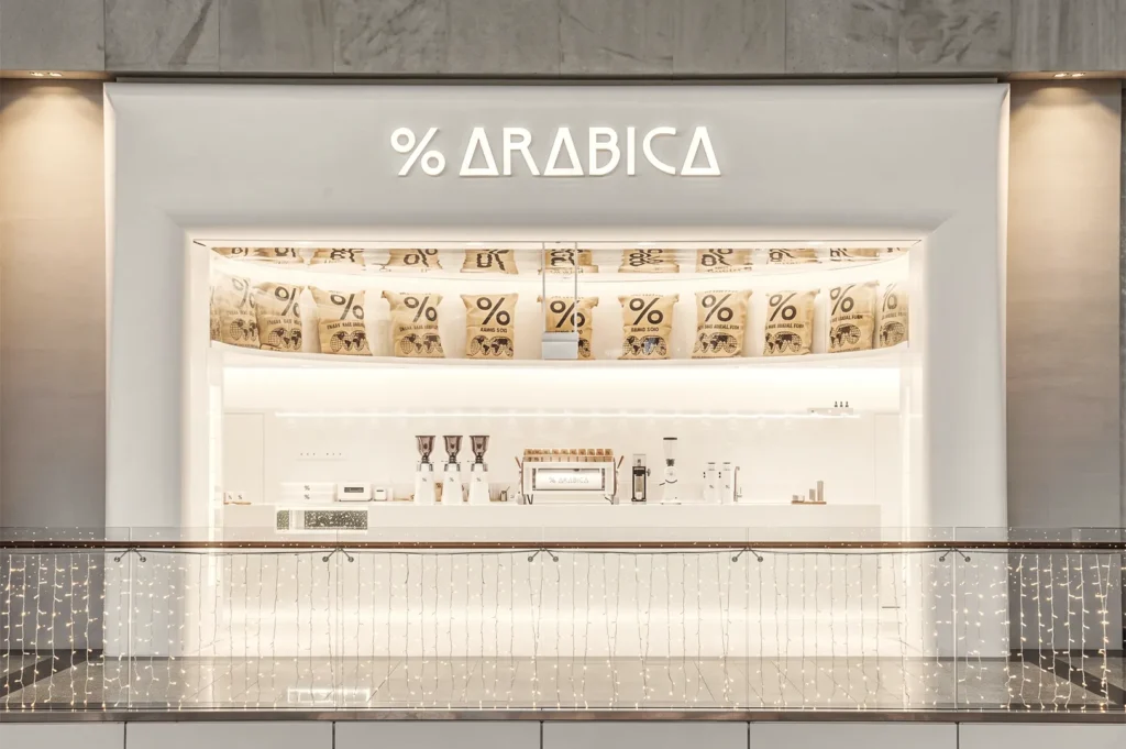 Minimalist % Arabica Singapore coffee shop with white modern design, espresso machines, and branded coffee bags on display.